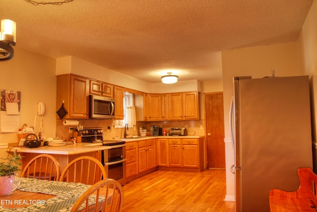 kitchen with a textured ceiling, stainless steel appliances, a sink, light wood-style floors, and light countertops