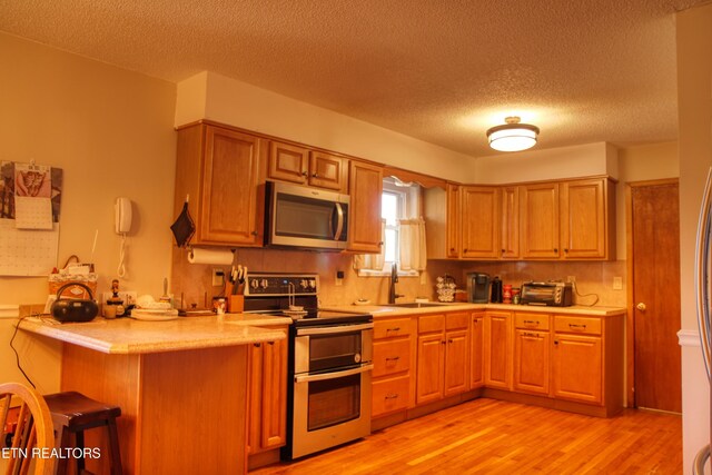 kitchen with a breakfast bar area, a peninsula, stainless steel appliances, light countertops, and light wood-type flooring