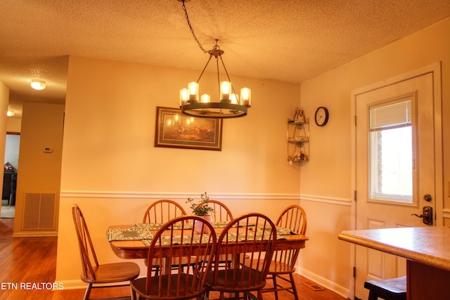 dining room with visible vents, an inviting chandelier, a textured ceiling, wood finished floors, and baseboards