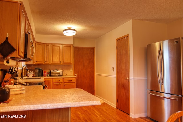 kitchen with light countertops, light wood-style flooring, appliances with stainless steel finishes, a textured ceiling, and a peninsula