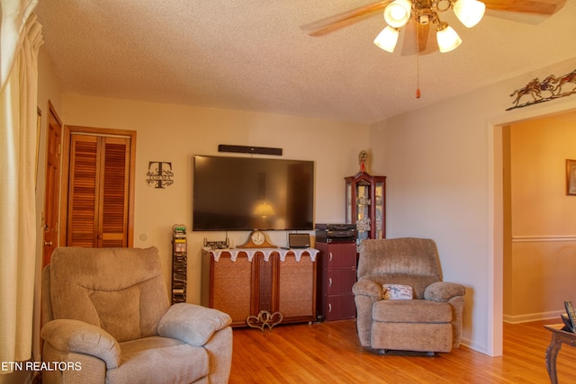 living area with a textured ceiling, wood finished floors, a ceiling fan, and baseboards