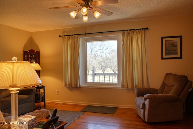 interior space with ceiling fan, a textured ceiling, baseboards, and wood finished floors