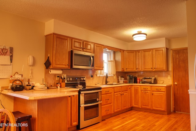 kitchen with a peninsula, light wood-style floors, light countertops, appliances with stainless steel finishes, and a kitchen bar