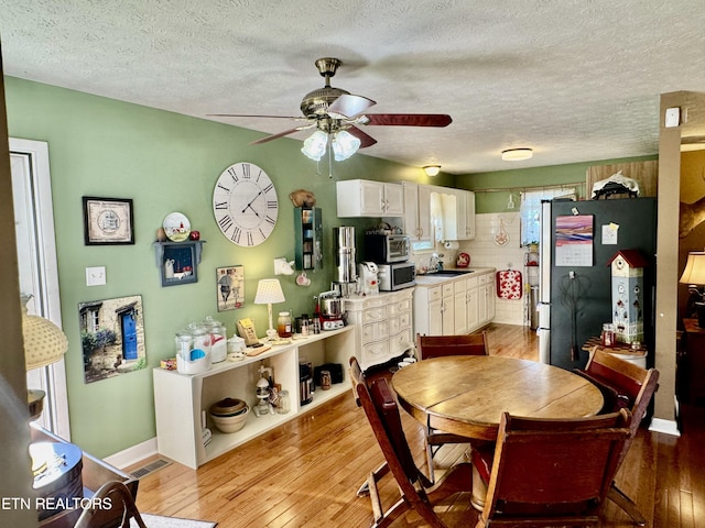 dining area with a textured ceiling, a ceiling fan, light wood-style flooring, and baseboards