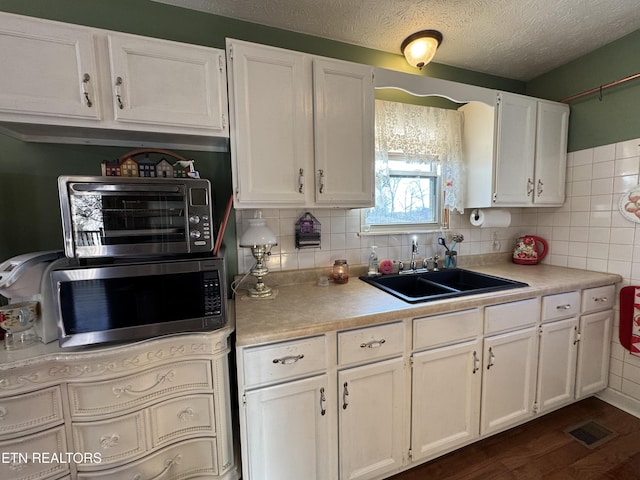 kitchen with light countertops, a sink, stainless steel microwave, and white cabinetry