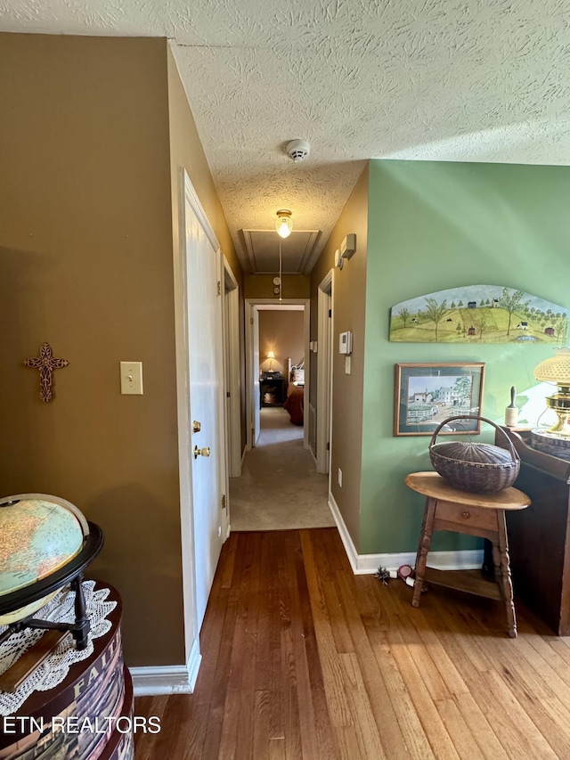 corridor featuring a textured ceiling, hardwood / wood-style floors, attic access, and baseboards