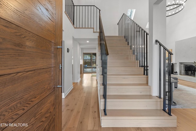 staircase with a chandelier, baseboards, a high ceiling, and hardwood / wood-style floors