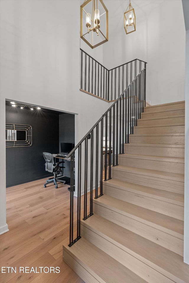 stairs with a notable chandelier, a high ceiling, and wood finished floors