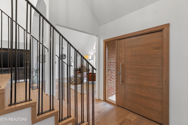 foyer entrance with stairs, lofted ceiling, and wood finished floors