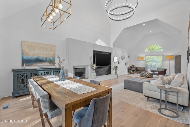 dining area with a chandelier, high vaulted ceiling, light wood-style flooring, visible vents, and baseboards