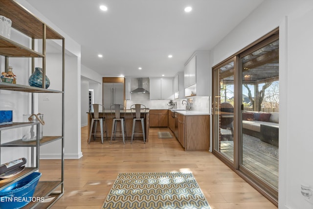 kitchen with wall chimney exhaust hood, recessed lighting, light countertops, and light wood-style floors