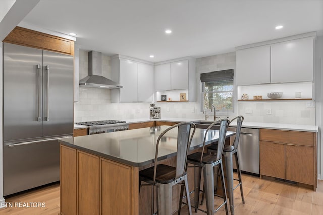 kitchen with light wood-style flooring, appliances with stainless steel finishes, a breakfast bar area, wall chimney range hood, and open shelves