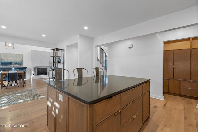 kitchen featuring light wood-style flooring, recessed lighting, a center island, dark countertops, and a glass covered fireplace