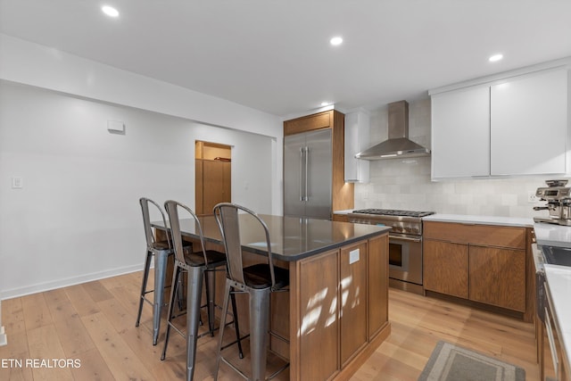 kitchen with decorative backsplash, premium appliances, wall chimney exhaust hood, a breakfast bar, and light wood-type flooring