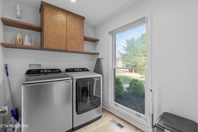 clothes washing area featuring light wood-style floors, washer and dryer, cabinet space, and visible vents