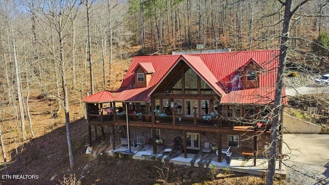 rear view of house featuring metal roof, a patio, and a view of trees