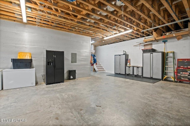 garage with black refrigerator with ice dispenser, fridge, electric panel, and concrete block wall