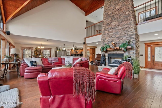 living area featuring a stone fireplace, hardwood / wood-style floors, beamed ceiling, and a notable chandelier