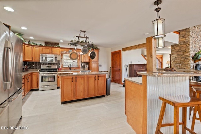 kitchen featuring brown cabinetry, decorative backsplash, decorative light fixtures, a center island, and stainless steel appliances