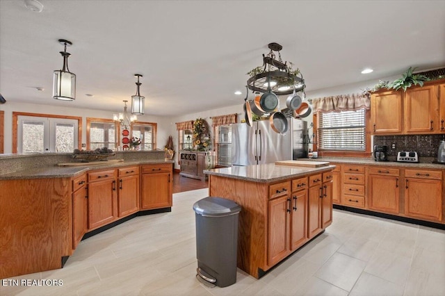 kitchen with a kitchen island, hanging light fixtures, backsplash, freestanding refrigerator, and brown cabinets