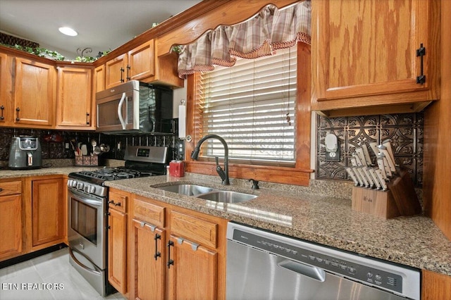 kitchen featuring decorative backsplash, brown cabinetry, light stone countertops, stainless steel appliances, and a sink