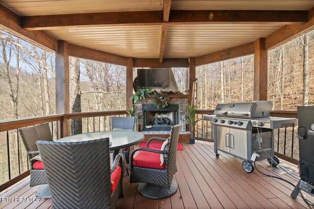 wooden deck with outdoor dining space, an outdoor stone fireplace, and a grill