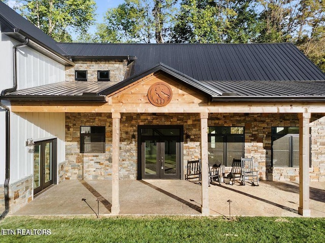 rear view of property featuring stone siding, a standing seam roof, a patio, and french doors