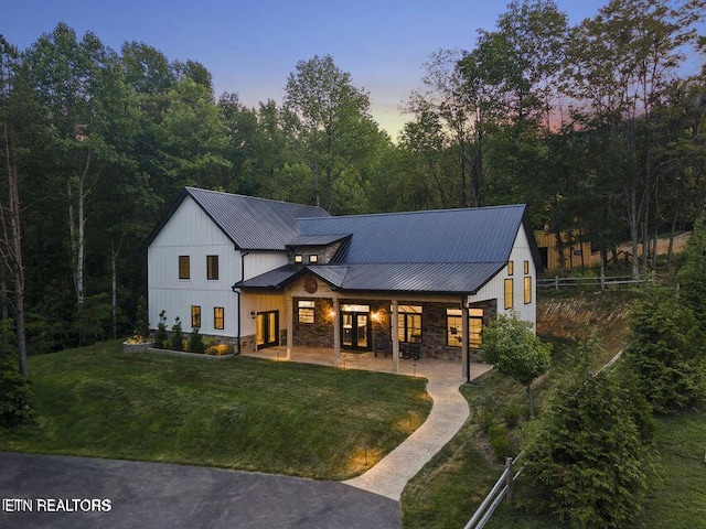 modern farmhouse style home with a lawn, a patio, stone siding, metal roof, and fence