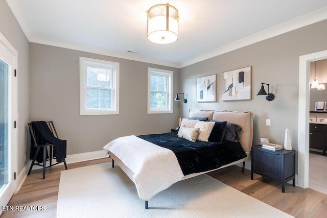 bedroom featuring crown molding, light wood finished floors, connected bathroom, a sink, and baseboards