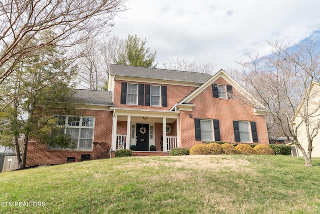 traditional-style home featuring brick siding, covered porch, a front lawn, and a shingled roof