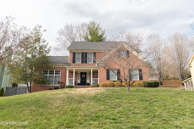 view of front of house featuring brick siding, covered porch, a front lawn, and fence