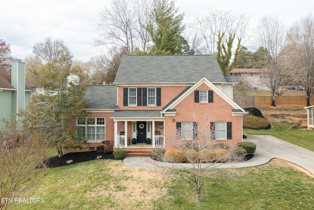 view of front facade with brick siding, concrete driveway, a front yard, roof with shingles, and covered porch