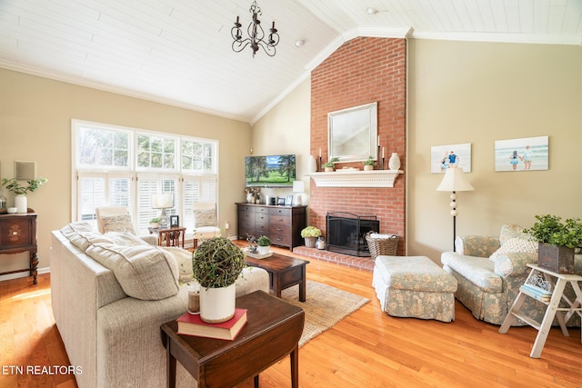 living room with wood finished floors, ornamental molding, vaulted ceiling, a brick fireplace, and a notable chandelier