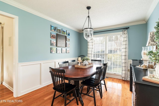 dining space featuring a wainscoted wall, a textured ceiling, light wood-type flooring, and ornamental molding