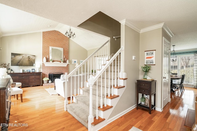 stairs with an inviting chandelier, a brick fireplace, wood finished floors, and crown molding