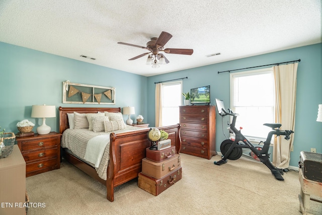 bedroom with visible vents, light colored carpet, a ceiling fan, and a textured ceiling