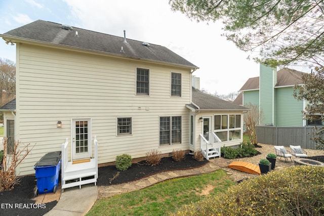 rear view of house featuring entry steps, fence, and a sunroom