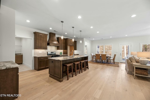 kitchen with a kitchen breakfast bar, dark brown cabinets, stainless steel range with gas cooktop, custom exhaust hood, and light wood finished floors