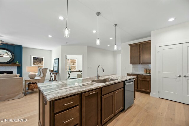 kitchen with a fireplace, a sink, light wood-style flooring, and stainless steel dishwasher