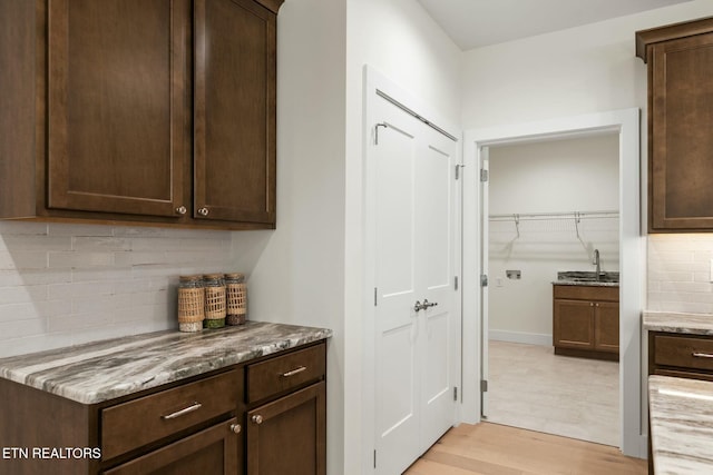 interior space featuring dark brown cabinets, light stone counters, a sink, and light wood-style flooring