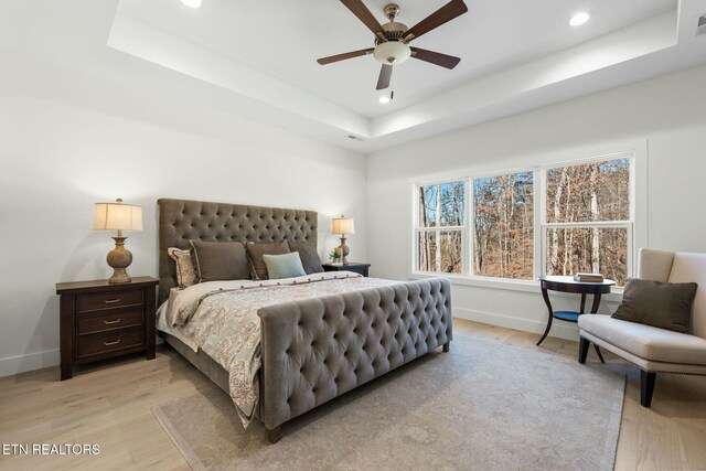 bedroom with ceiling fan, recessed lighting, baseboards, light wood-type flooring, and a tray ceiling