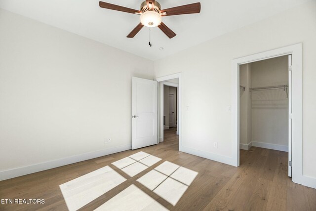 unfurnished bedroom featuring a spacious closet, a closet, light wood-type flooring, and baseboards