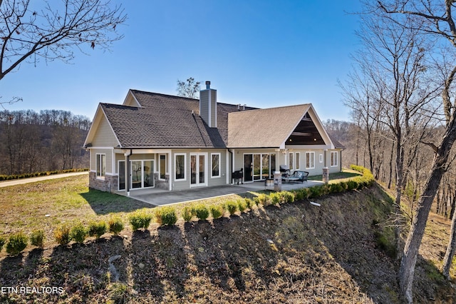 rear view of house with a patio area, a shingled roof, and a chimney