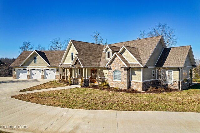 craftsman inspired home with roof with shingles, an attached garage, a front yard, stone siding, and driveway