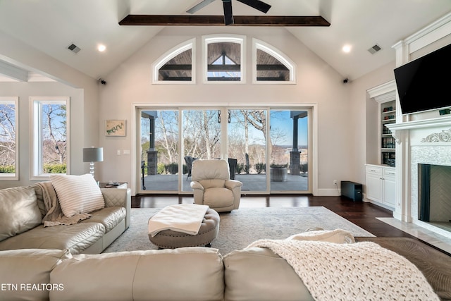 living room featuring plenty of natural light, visible vents, dark wood-style floors, beamed ceiling, and a fireplace