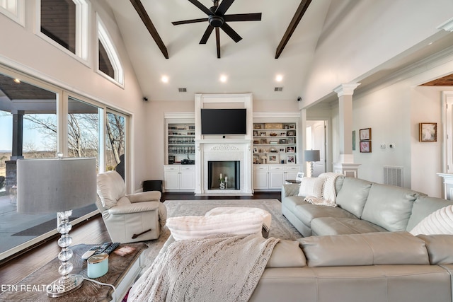 living area featuring ornate columns, ceiling fan, beamed ceiling, and wood finished floors