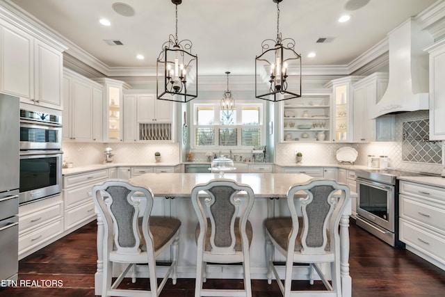 kitchen featuring dark wood finished floors, stainless steel appliances, visible vents, a kitchen island, and premium range hood