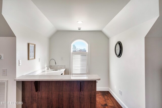 kitchen featuring lofted ceiling, a peninsula, a breakfast bar, a sink, and light countertops