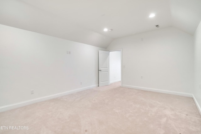 empty room with vaulted ceiling, light carpet, visible vents, and baseboards