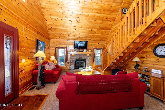 carpeted living room with wooden walls, wooden ceiling, stairway, a fireplace, and high vaulted ceiling